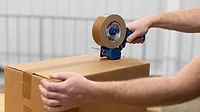Worker sealing a corrugated shipping box with a hand tape dispenser.