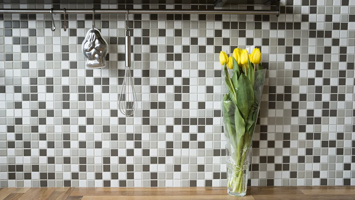 Alt text: Black, white and gray peel and stick tile in a kitchen with yellow flowers in a vase 