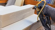 Spraying adhesive glue onto foam pieces in manufacturing factory