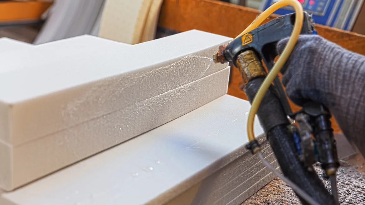 Spraying adhesive glue onto foam pieces in manufacturing factory