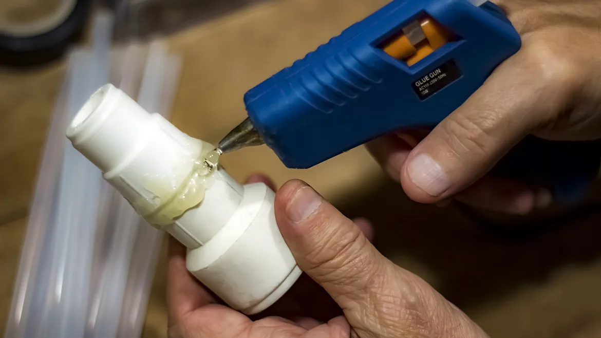Male using glue gun to fix a plastic pipe part