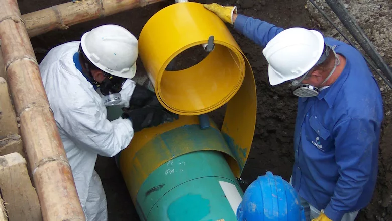 Photo of two men in hardhats installing pipe