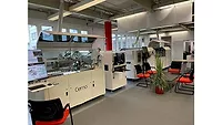 Nordson facility - A line of industrial equipment in a room, with a seating area and plants nearby.