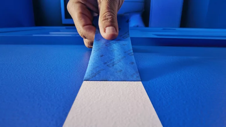 Picture of tape being pulled off a surface revealing a white line on blue background