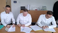 Picture of three men sitting at a table and signing documents