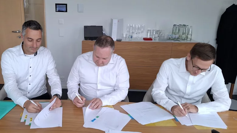 Picture of three men sitting at a table and signing documents