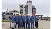 Picture of 12 people in blue shirts standing in front of a chemical facility