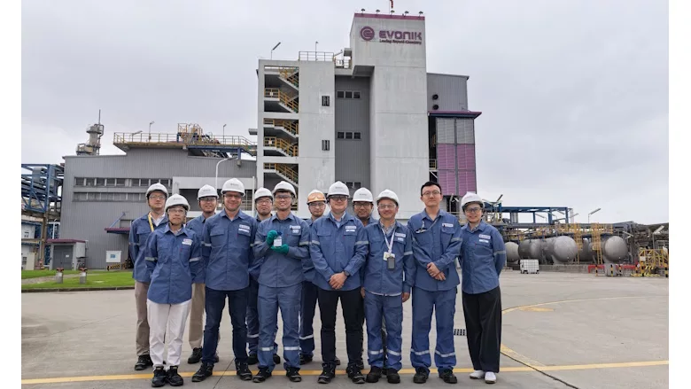 Picture of 12 people in blue shirts standing in front of a chemical facility