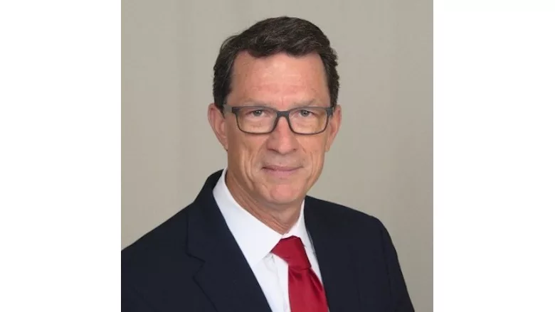 Picture of a man in a dark suit with a white shirt and red tie.