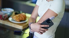A person with a medical monitoring device on their arm holding a cell phone next to it. 