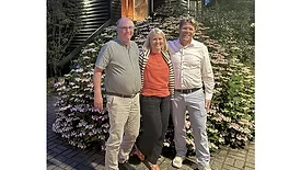 Picture of two men and a woman standing in front of a flower bush