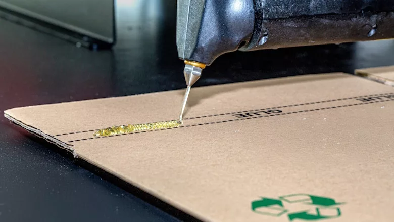 Picture of hot-melt adhesive being applied to cardboard box