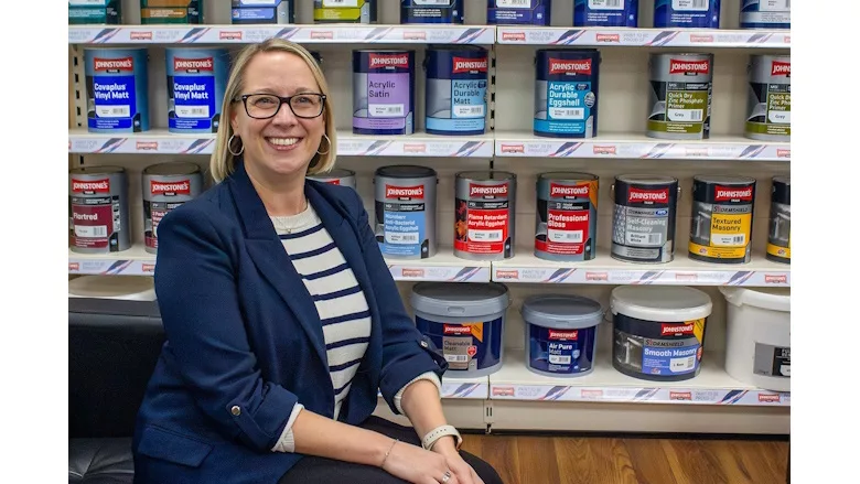 A picture of Sarah Trowse sitting in front of a shelf full of paint cans