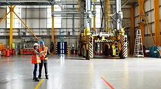Two people in safety vests standing near the doors of a modern warehouse.
