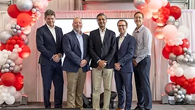 Picture of four men standing under an arch or red and pink balloons