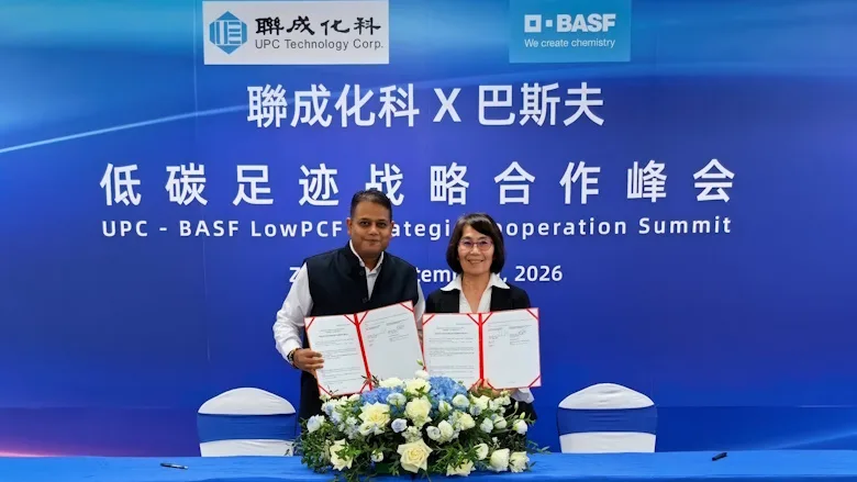 A woman and a man standing in front of a blue backdrop holding signed documents