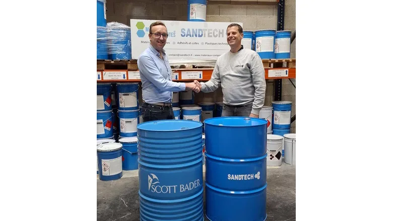 Picture of two men shaking hands in front of large blue drum containers
