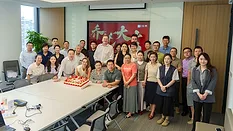Picture of a group of people around a table with a cake on it